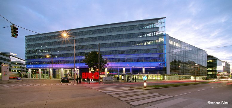 Exterior view of the glass-facade Am Europlatz 2 / EP 4 building at dusk with blue lighting.