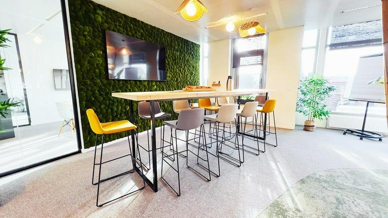 Meeting room with a long high table, yellow stools, and a lush green moss feature wall at Chaussée de Wavre 1110.