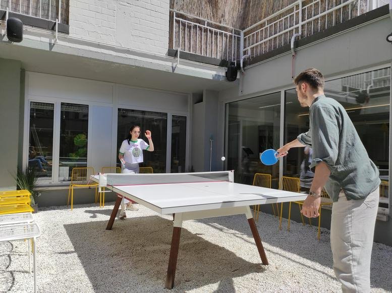 A man and woman play table tennis in a sunlit outdoor courtyard at Eedverbondkaai 242, Ghent.