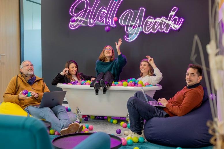 Casual meeting space with people in a ball pit under a neon sign.