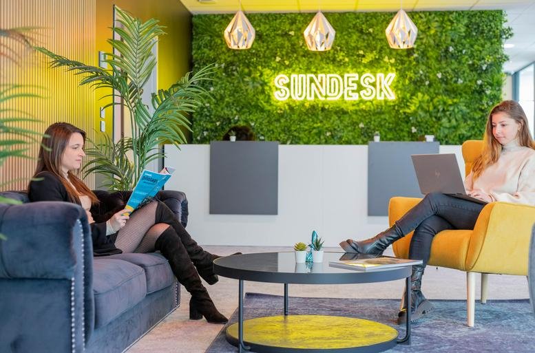 Vibrant reception area at Emerald Square with a green living wall and neon sign.