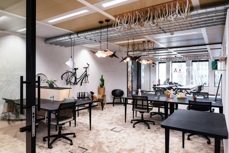 Spacious communal coworking area at Esplanade Simone Veil 1, Liege with industrial ceilings and bicycle wall art.