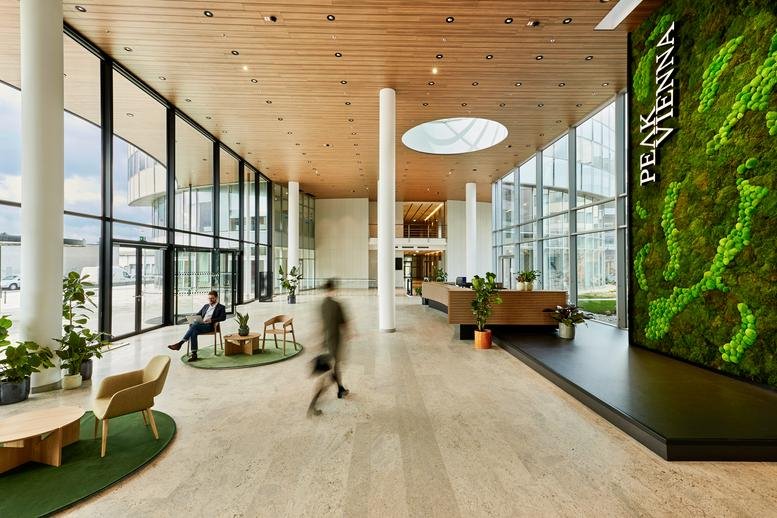 Spacious lobby at Peak Vienna with high ceilings, wooden panels, and a large green moss wall.