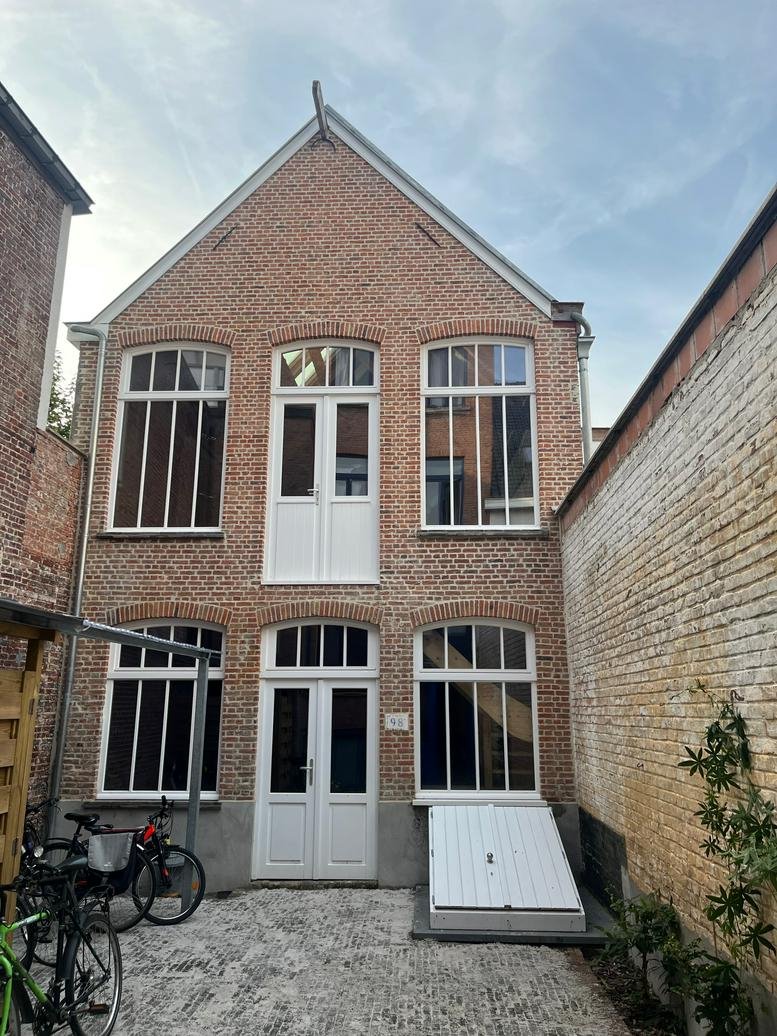 Exterior view of the brick building at Holstraat, Ghent, Belgium with large windows and white doors.