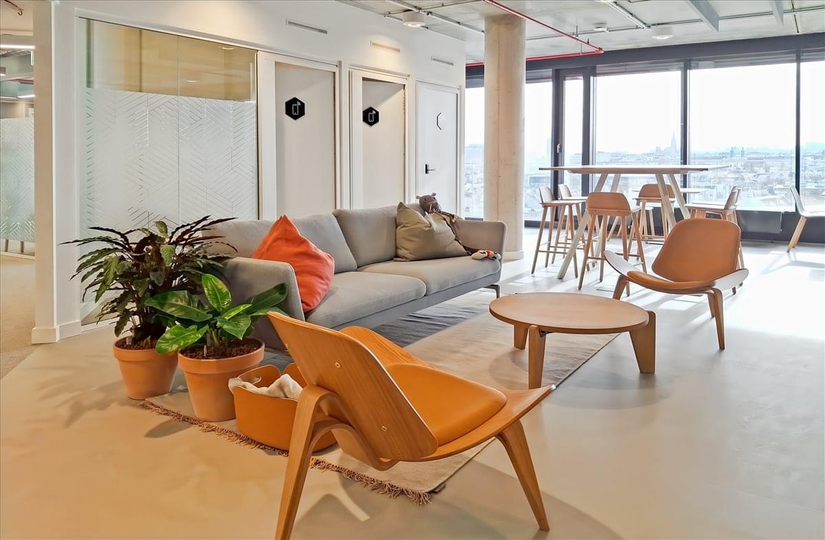 Spacious communal lounge with grey sofa and orange accents at Franz-Josefs-Bahnhof, Julius-Tandler-Platz 3.