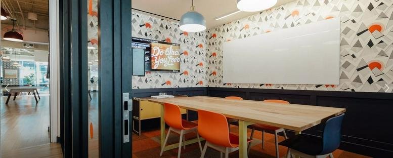 Spacious meeting room at La Nef des Collines de l’Arche featuring orange chairs and patterned wallpaper.