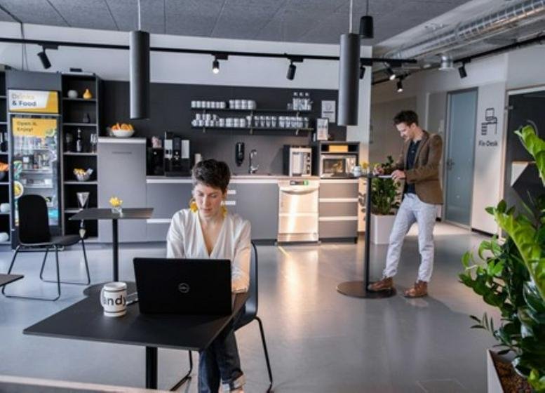 Common area featuring a kitchen, high tables, and a person working on a laptop.