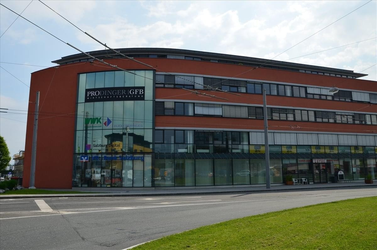 Exterior view of the curved brick and glass building at Karolingerstrasse 1, Salzburg.