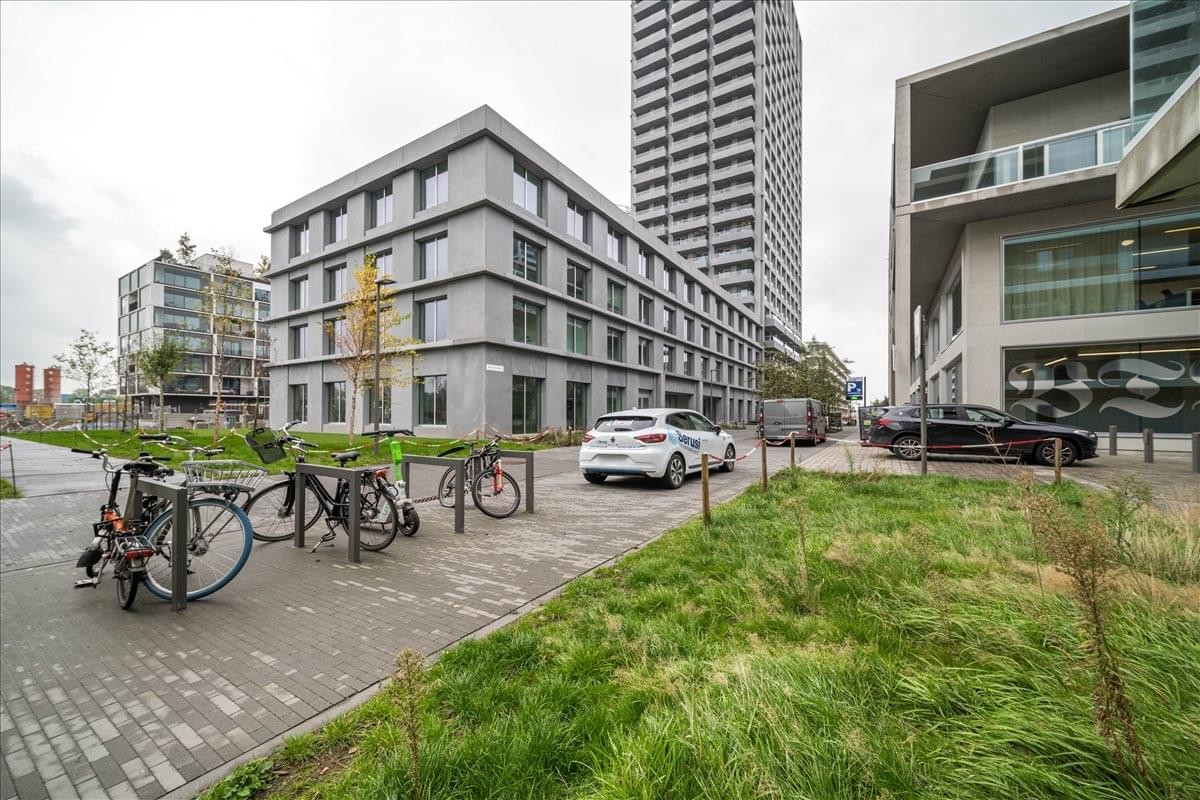 Modern grey exterior of the Michel De Braeystraat 52 building with a paved walkway and bicycle racks.