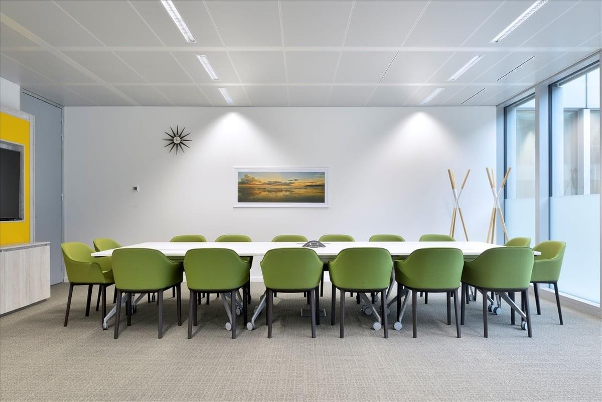 Spacious boardroom at Rue de Venise 21 featuring a long white table and lime green chairs.