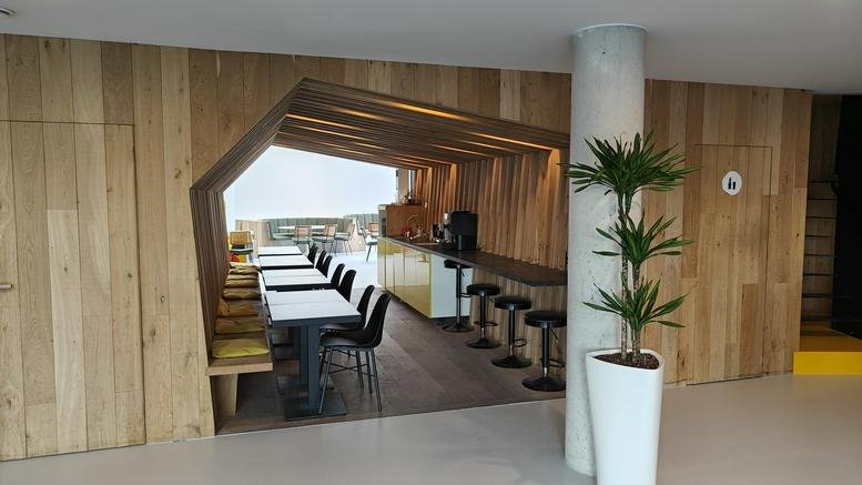 Modern wooden breakout area with dining tables and a tall potted plant at Stationsplein 29, Sint-Niklaas.