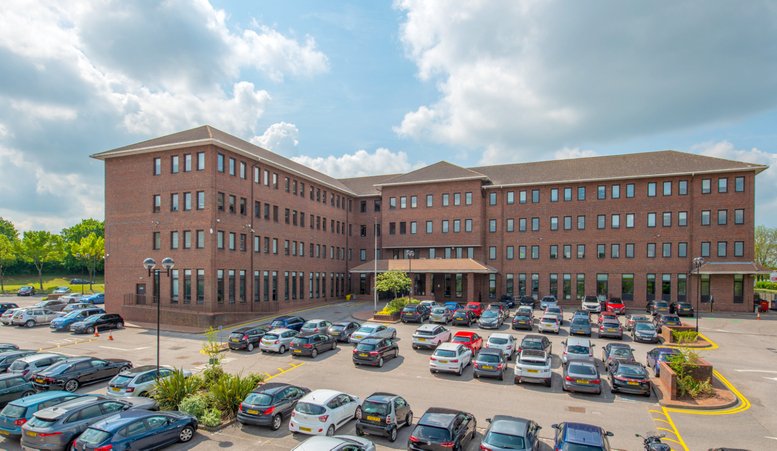 Exterior view of the brick facade at One, Station Approach, featuring a large parking area under a bright sky.