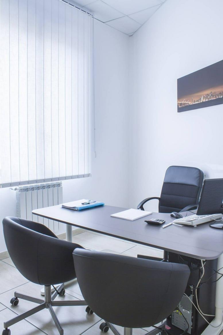 Private office at Piazza Carità, featuring two dark armchairs and a desk with a laptop near a large window.
