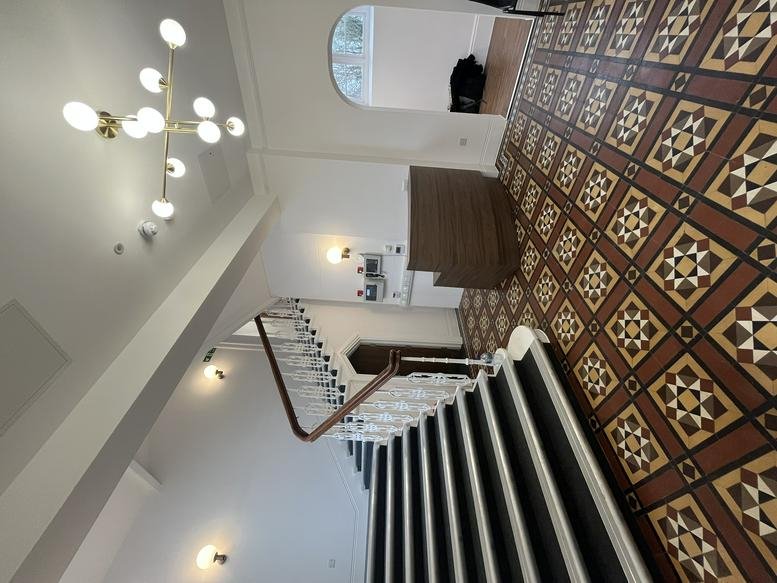 Elegant stairway with patterned tile floor and modern chandelier at Queen Victoria House.