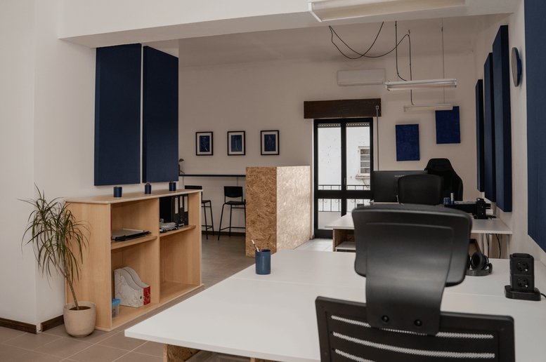 Spacious open-plan workspace at Rua Cândido dos Reis, 7B, with white desks, blue acoustic panels, and potted plants.