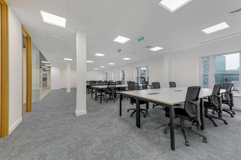 Spacious office layout with large windows and multiple grey workstations.