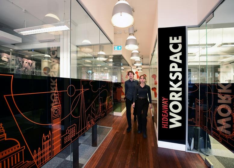 A hallway at 1 Empire Mews, London with glass walls, wood flooring, and Hideaway Workspace signage.