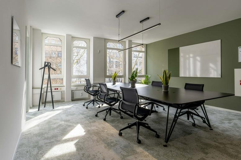 Large meeting room featuring minimalist black chairs and a green wall.
