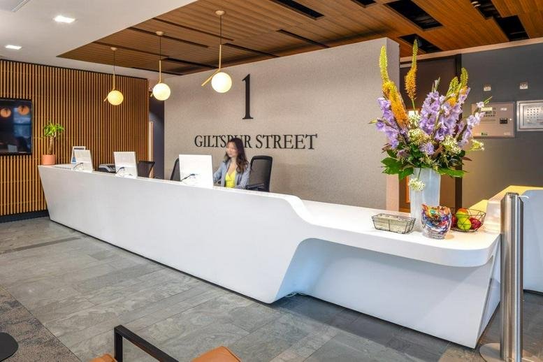 White minimalist reception desk at 1 Giltspur Street, London with vibrant purple flowers.