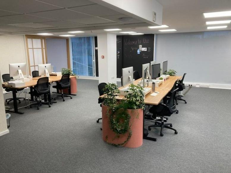Bright office area with wooden desks, potted plants, and multiple computer monitors.
