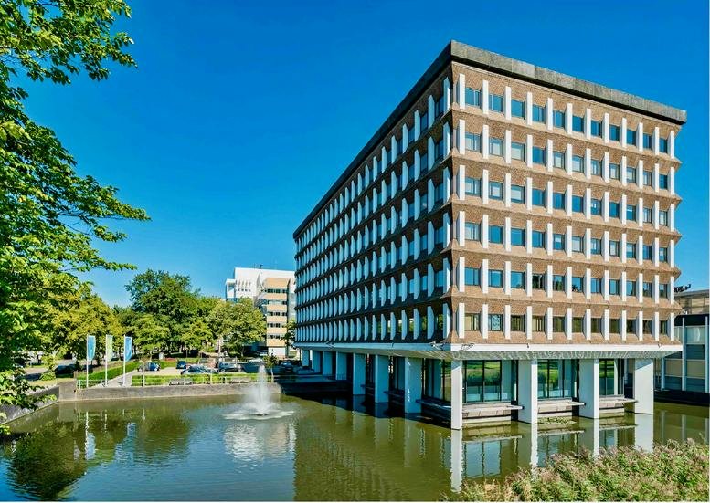 Exterior view of the brick and glass Kronenburg building reflecting in a surrounding pond with a fountain.