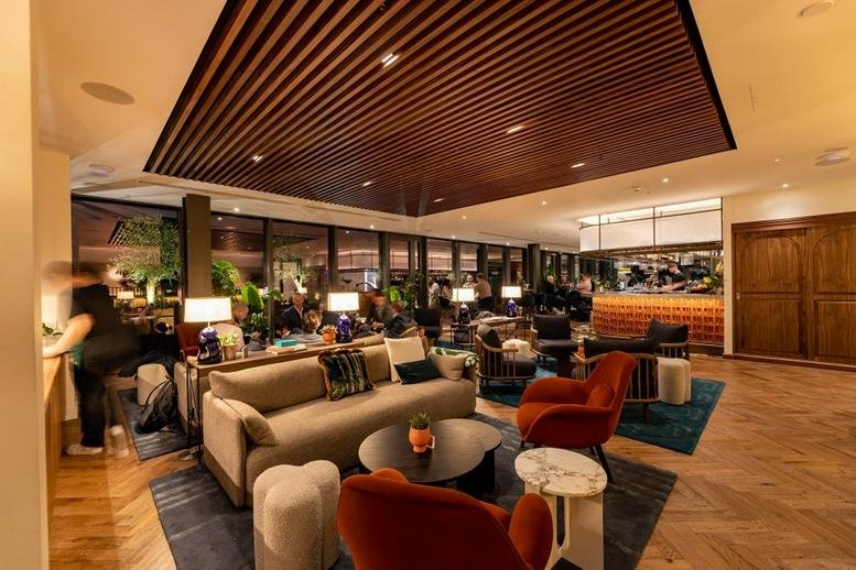 Warmly lit lounge at 103 Colmore Row with velvet armchairs, plush sofas, and a wood-slat ceiling.