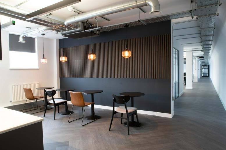 Communal breakout area with cafe tables, leather chairs, and wood-slat feature wall at Artillery House.