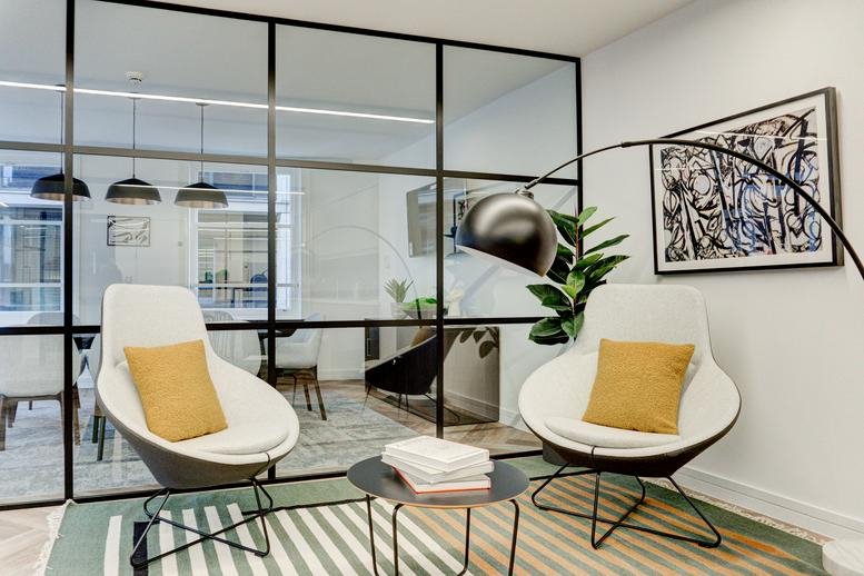 A modern lounge at 11 Cursitor Street featuring white pod chairs, yellow pillows, and a black framed glass partition.