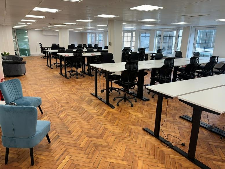 Spacious open-plan workspace with parquet flooring and blue armchairs.