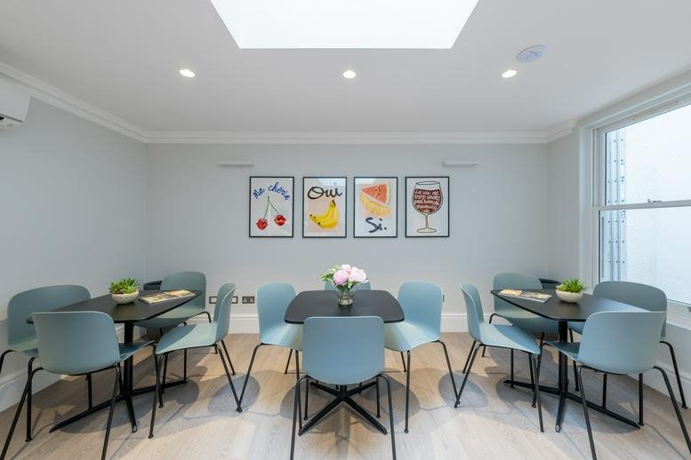 Communal dining area with blue chairs and colorful fruit-themed wall art.