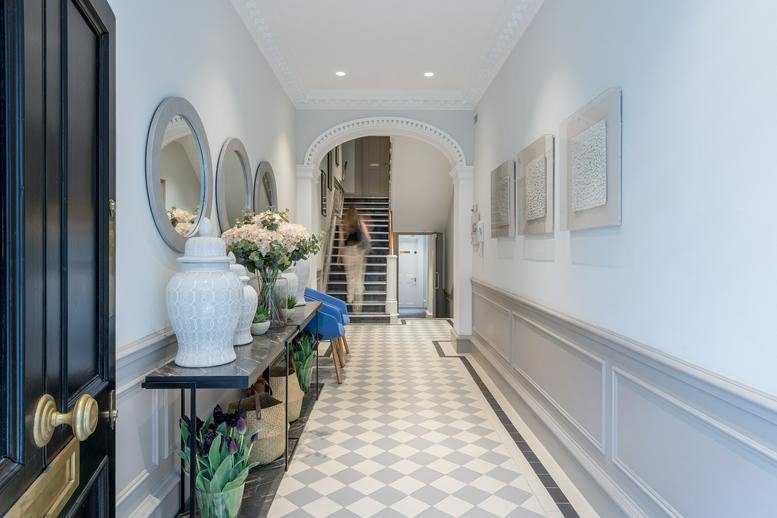 Elegant entrance hallway with checkered tile flooring, white vases, and decorative wall molding.