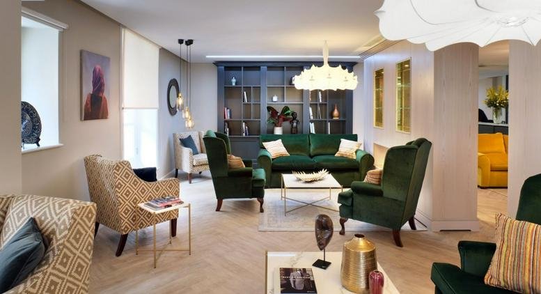Spacious lounge area with green velvet armchairs and a blue built-in bookcase.