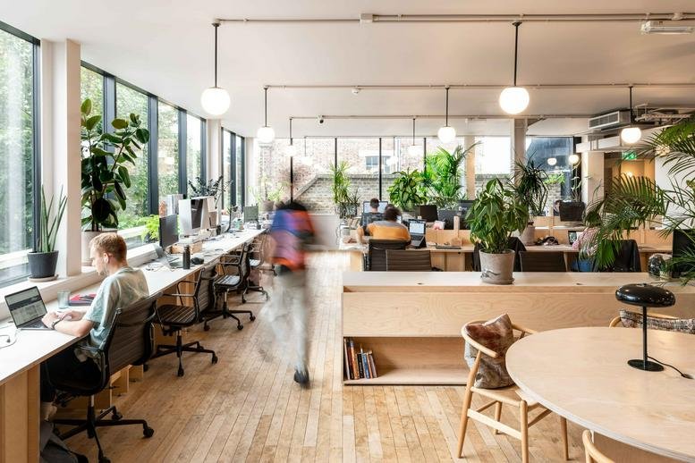 Spacious open-plan workspace at 133a Rye Lane, Peckham with long white desks and abundant indoor plants.