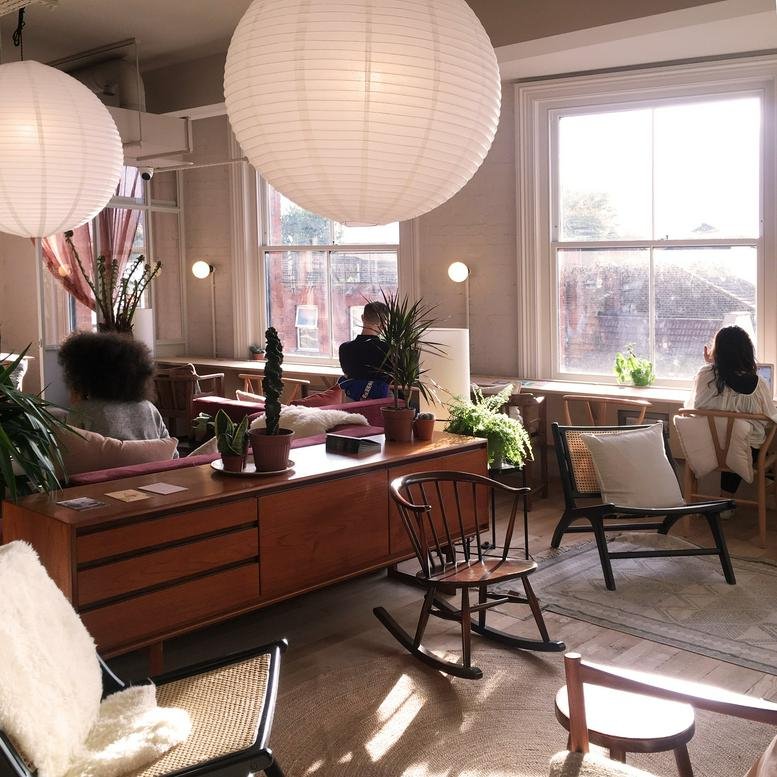 Sunlit lounge area featuring mid-century modern furniture, paper lanterns, and indoor plants.