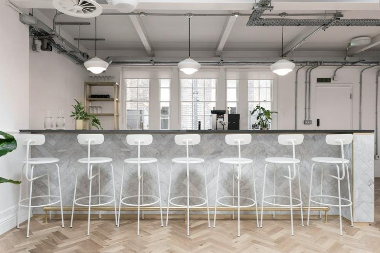 Communal breakout area featuring a grey marble bar with white high stools and hanging pendant lights.