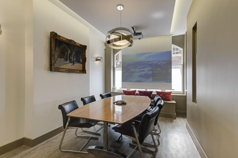 Professional meeting room featuring a wooden oval table, black leather chairs, and a projection screen.