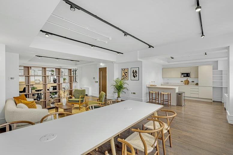 Open breakout space with white dining tables, a lounge area, and a kitchen.