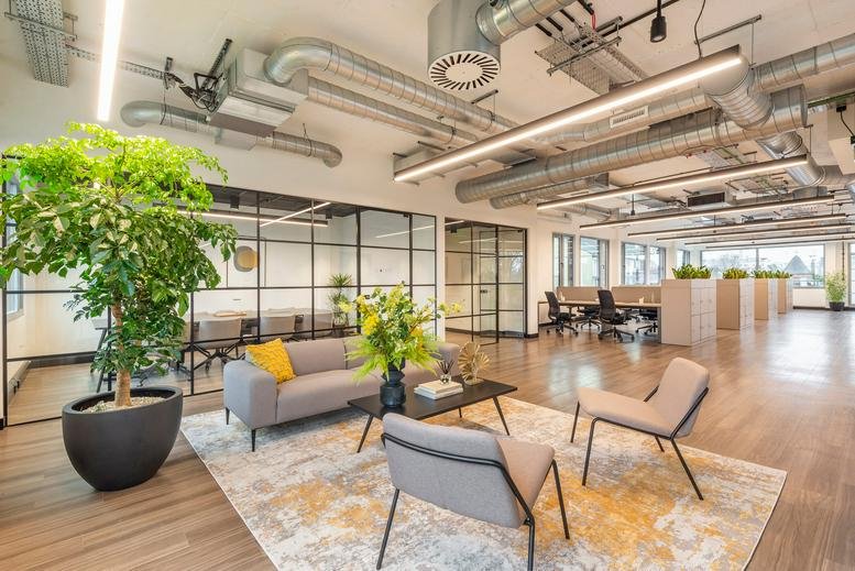 Modern lounge area at 147 Arlington Road with grey sofas, vibrant plants, and industrial-style ceilings.