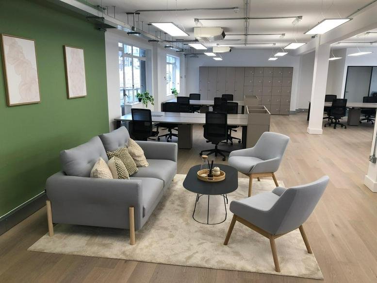 Sunlit lounge with grey armchairs, a sofa, and green wall accents.
