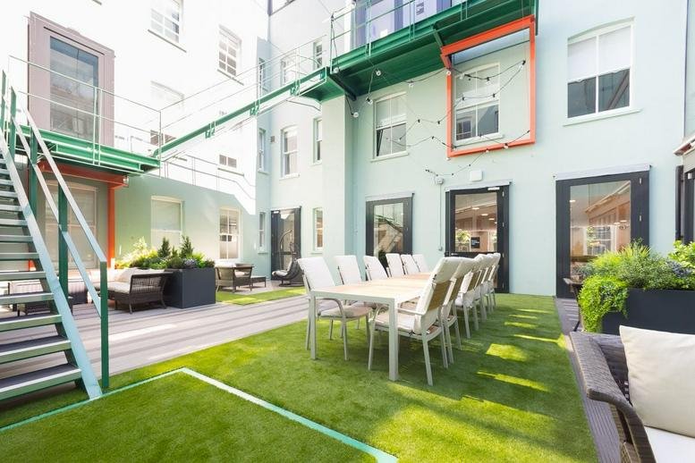 Sunny outdoor communal courtyard at 15 Alfred Place, Camden with artificial turf and dining tables.