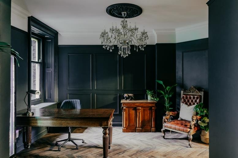 Elegant dark-paneled office at 15, Hanover Square, London with a large chandelier and wooden desk.