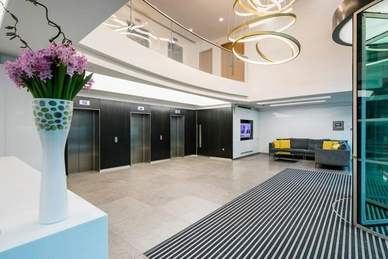 Bright modern lobby with a curved light fixture, marble floors, and lift access.