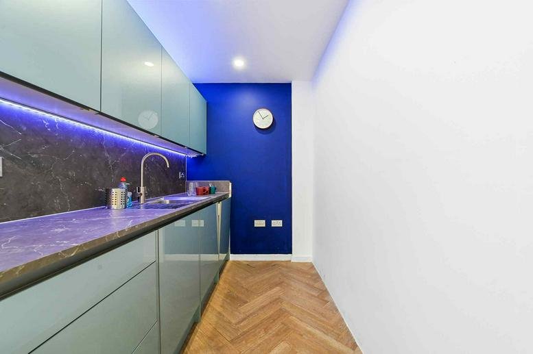 Sleek kitchenette with blue cabinetry, under-cabinet lighting, and a vibrant blue accent wall.