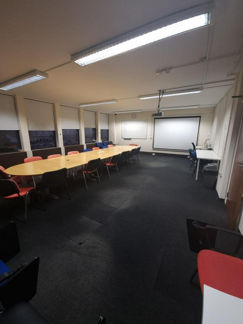 Spacious boardroom at Forest House with a long wooden table, black chairs, and a large projector screen.