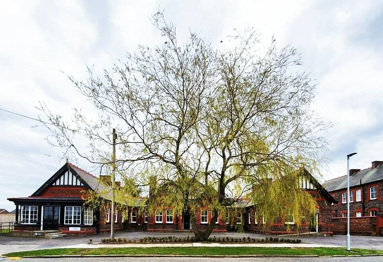 Exterior view of the historic brick building 16 Clock Tower Park with a large tree in front.
