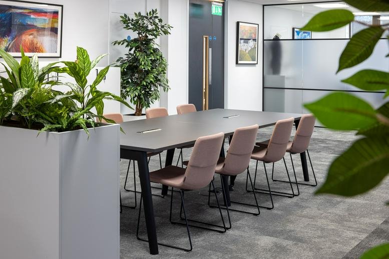 Modern conference room with a long dark table, pink upholstered chairs, and greenery.