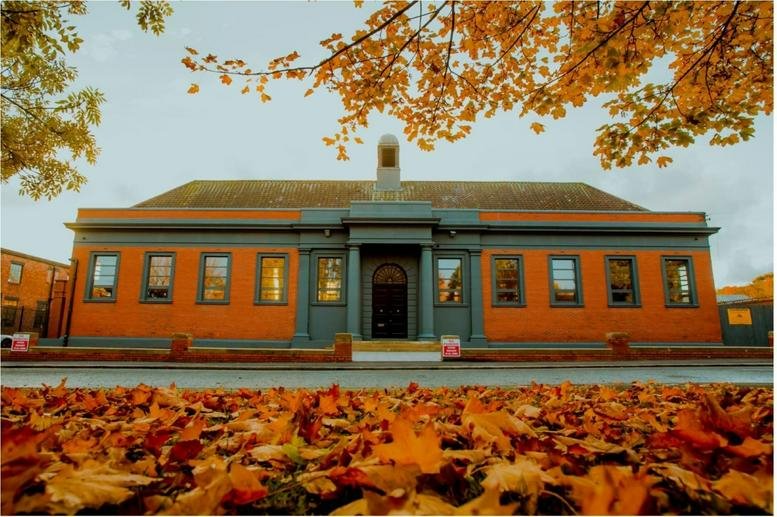 Exterior view of the historic red brick building at 168 Brinkburn Street with autumn leaves in the foreground.