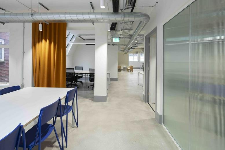 Bright workspace at 17 Aylesbury Street featuring a large white table, blue chairs and a mustard yellow curtain.