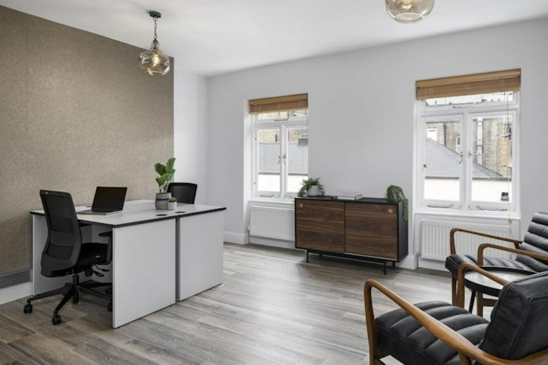 Spacious professional workspace at 17 Gosfield Street with double desks, wood furniture, and natural light.