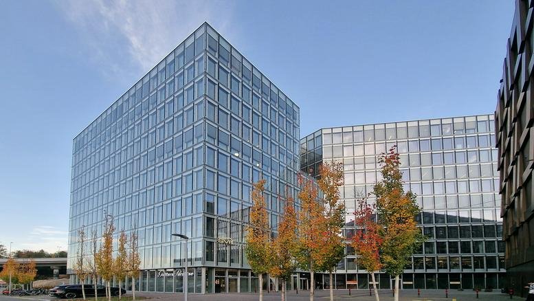 Exterior view of a large modern glass office complex with autumn trees.